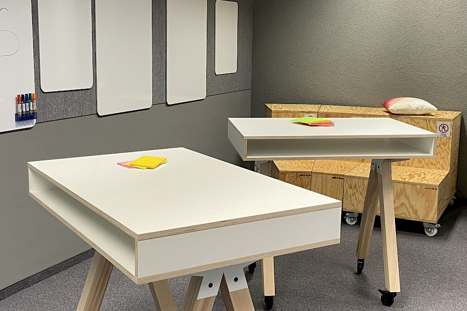 Zwei moderne Stehtische vor einer grauen Wand mit Pinnwänden