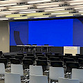 Ein großer Tagungsraum, in dem viele graue und schwarze Stühlen vor einer großen LED-Wall stehen