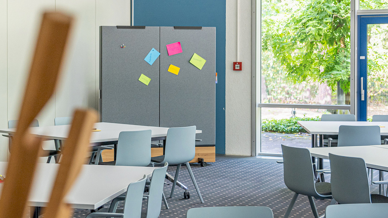 Moderner Seminarraum für Kick-off-Meetings mit flexibel angeordneten Tischen, Pinnwand mit bunten Moderationskarten und Blick ins Grüne.